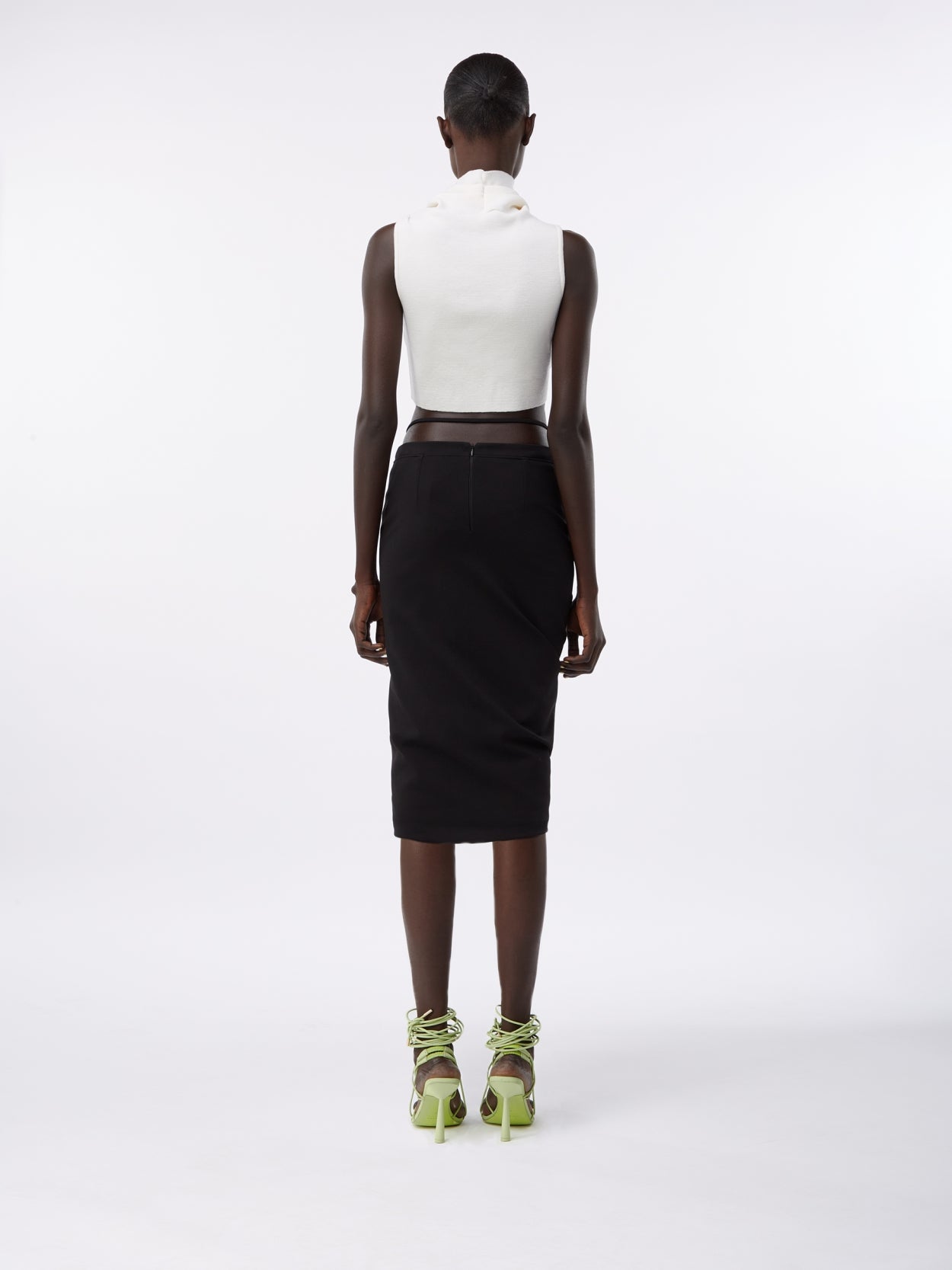 model wearing a white turtleneck wool crop top and a midi pencil skirt with waist strap
